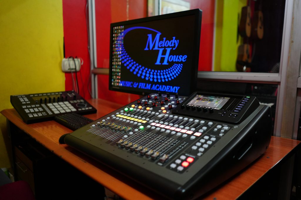A close-up shot of the Behringer X32 digital mixing console featuring motorized faders and an illuminated display, set up in the MFA sound engineering lab.