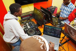 A high-angle shot of DJ students at Music And Film Academy Nairobi practicing on a professional Pioneer DJ setup with Rekordbox-linked laptops and monitors.