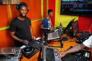 A high-angle view of two student DJs at Music And Film Academy Nairobi using Pioneer DJ controllers; one laptop displays a yellow Serato interface, and another shows a blue Rekordbox waveform screen.