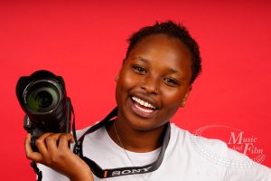 A smiling female student holding a professional Sony camera during a studio session at Music and Film Academy in Nairobi, illustrating how to buy photography gear in Nairobi.