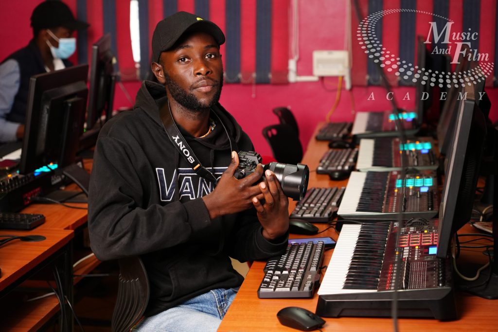 A student holding a Sony digital camera at a dedicated post-production workstation during practical video editing courses in Kenya.