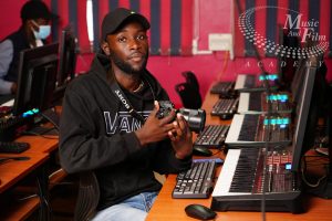 A student holding a Sony digital camera at a dedicated post-production workstation during practical video editing courses in Kenya.