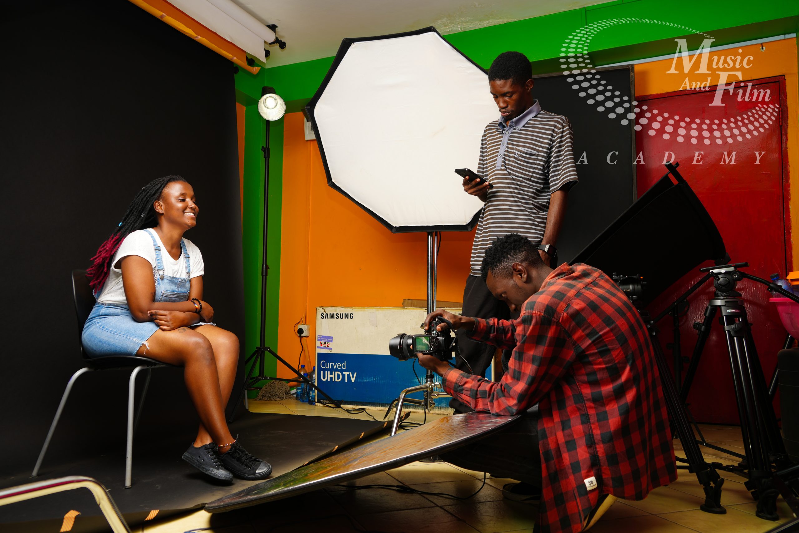 Students training on a live set at our film production school in Kenya, adjusting lighting modifiers and operating a digital cinema camera for a studio shoot.