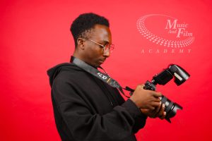 A male student reviewing commercial camera settings to build a photography portfolio for corporate clients during a practical studio session at the Music and Film Academy.