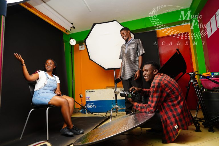 Film production students collaborating on creative set design and lighting placement to shoot high-end music videos on a budget at the Music and Film Academy studio.