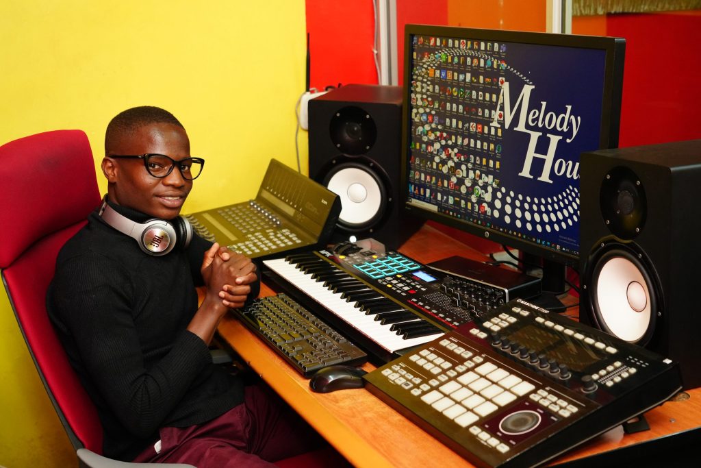 A student learning what is music production in a professional recording studio control room at the Music And Film Academy campus in Nairobi, surrounded by a MIDI keyboard, hardware production controllers, and studio monitors.